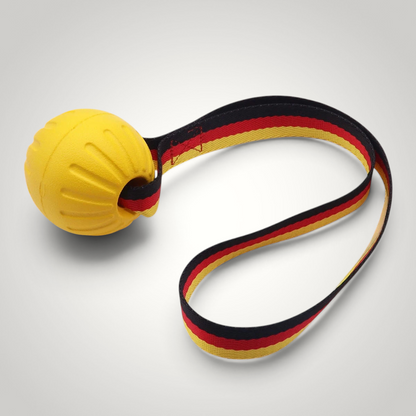 HappiFinds yellow EVA ball dog toy with a durable German flag patterned pull strap for tug and fetch play