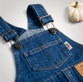HappiFinds blue cotton-denim dog overalls with adjustable metal straps and a front pocket on a rustic wooden table.