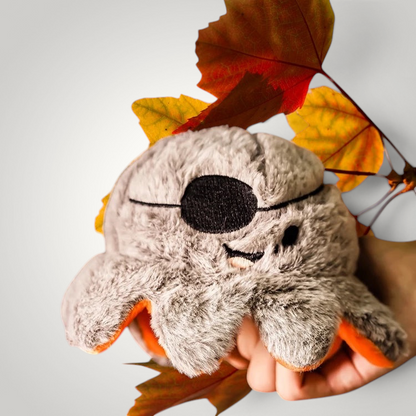 HappiFinds reversible plush pirate octopus toy with an eye patch, held in hand against a background of autumn leaves.